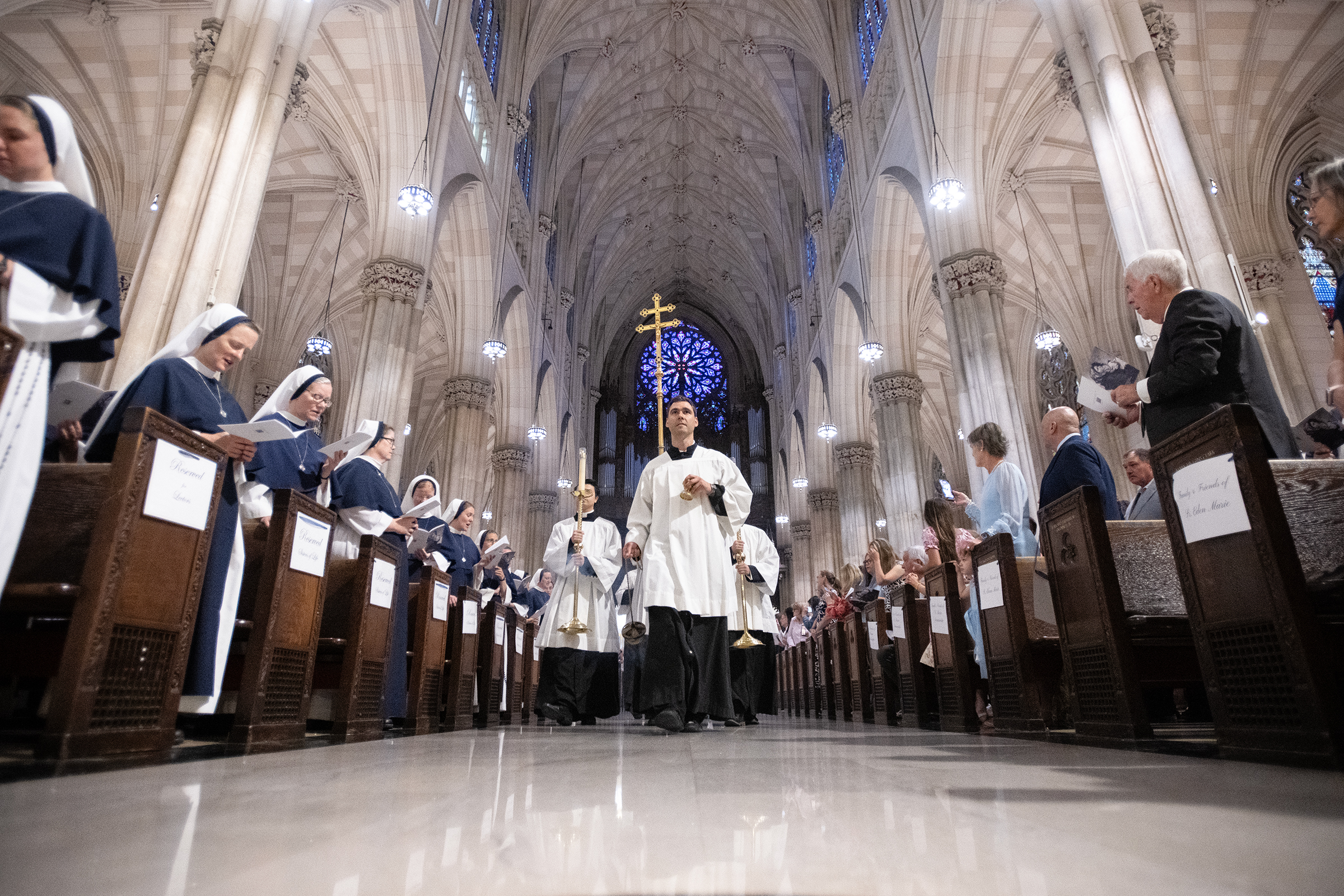 The processional cross and incense lead the entrance procession through St. Patrick’s Cathedral as Sisters and families look on