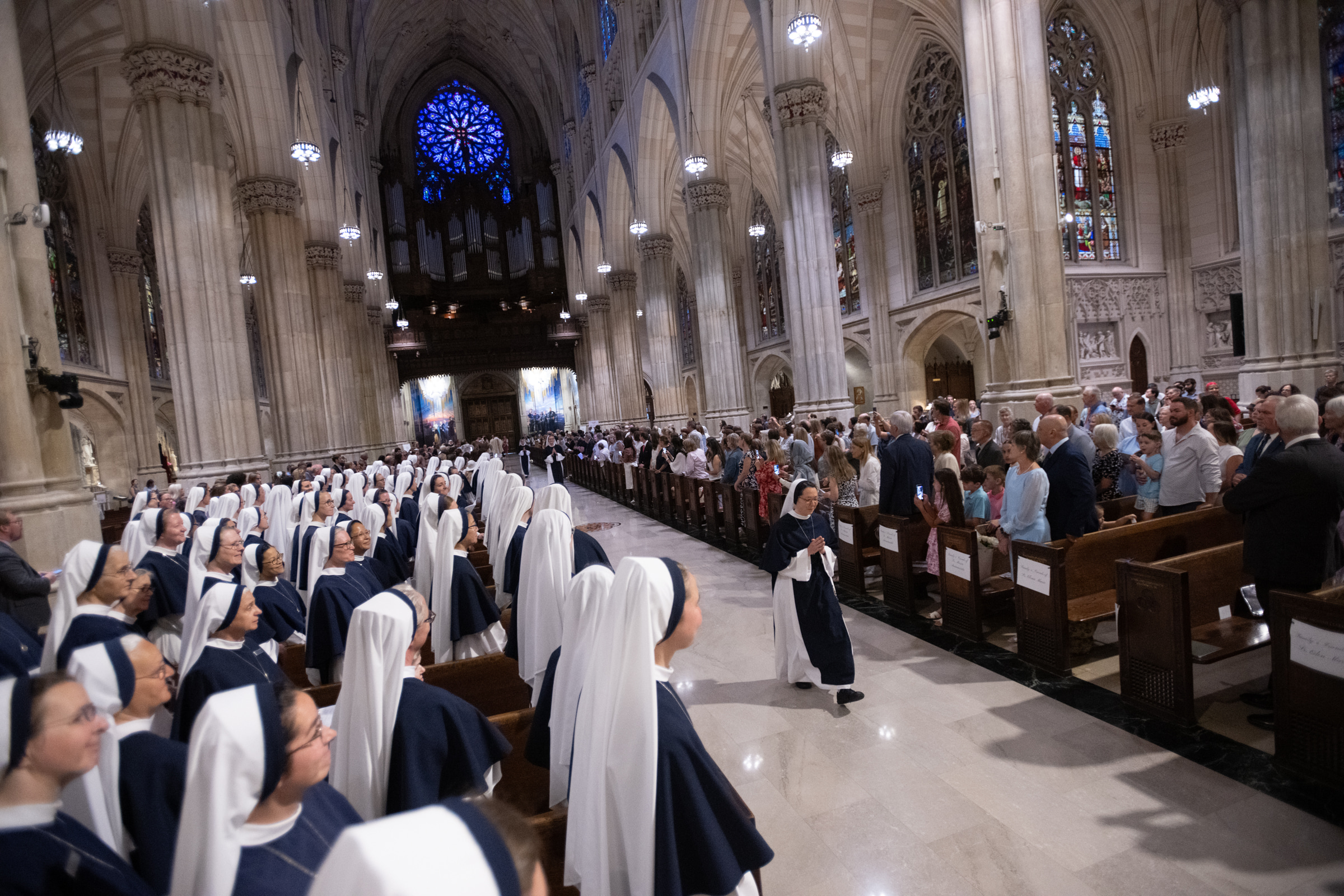 Sister Eden Marie, S.V., walks down the cathedral aisle as Sisters and guests look on.