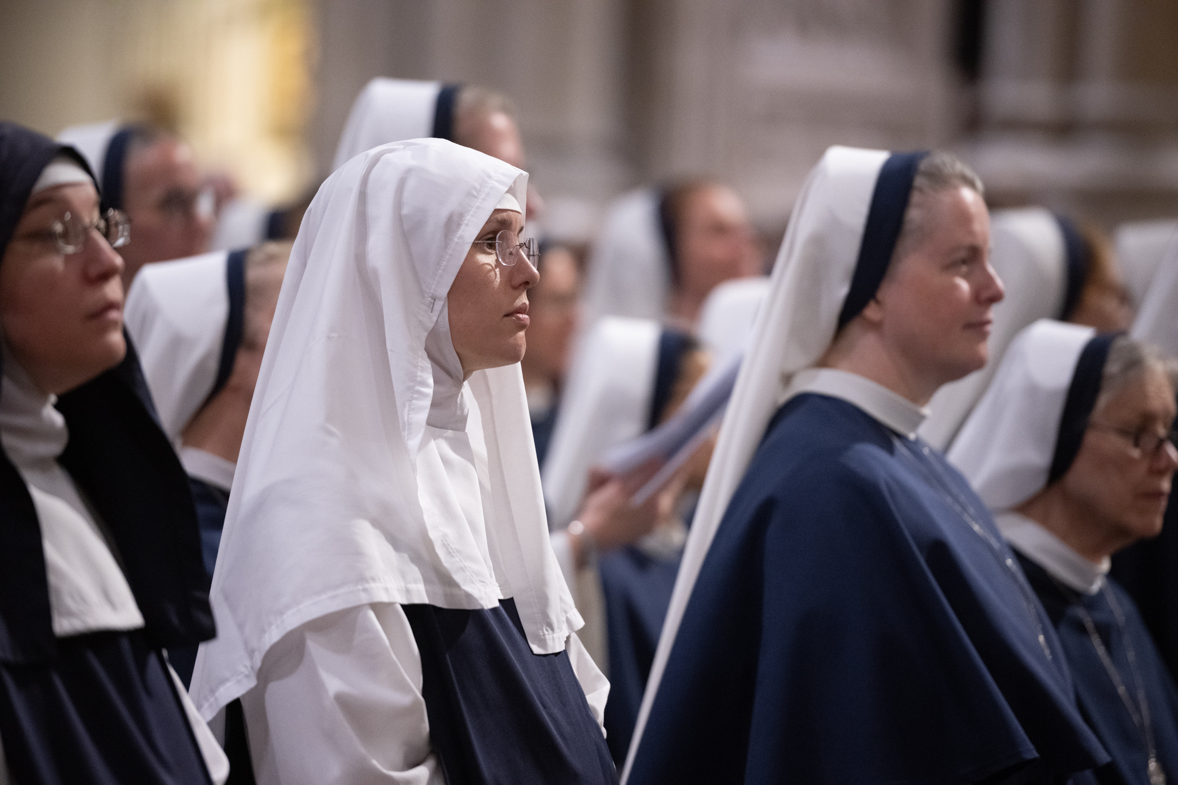 A Sister of Life in a white veil listens during Mass, surrounded by members of her community.