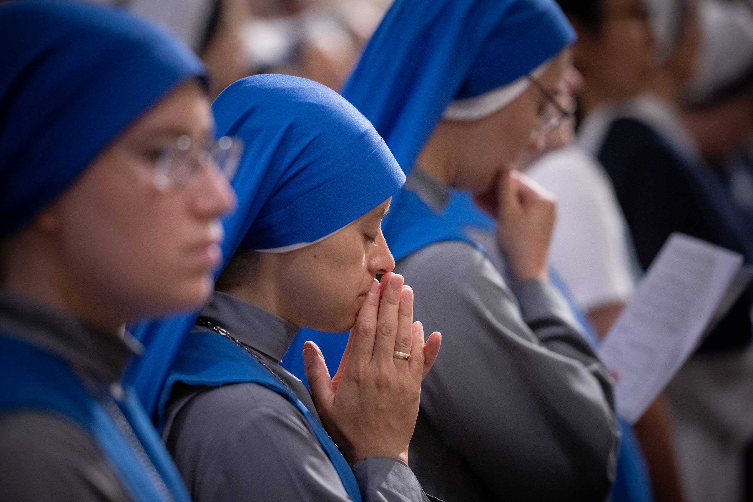 A woman religious in a bright blue veil prays with her eyes closed during Mass.