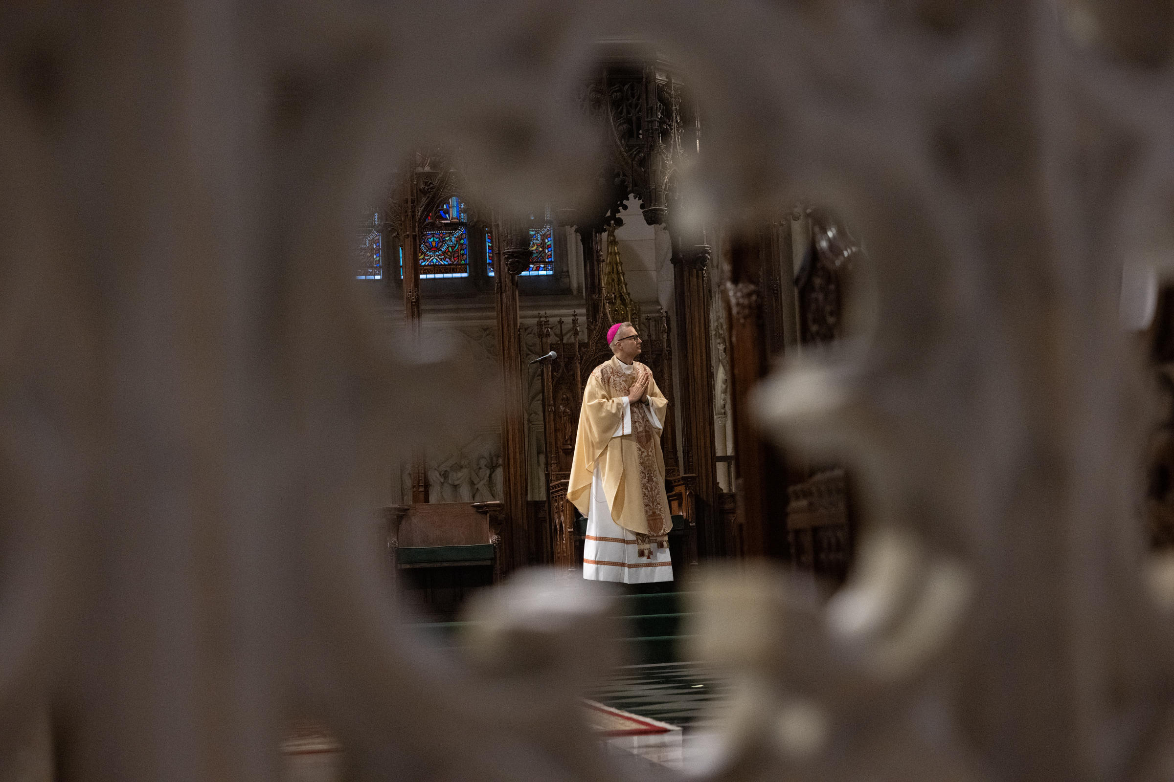 Archbishop Hicks stands in prayer in the sanctuary, framed between out-of-focus clergy.