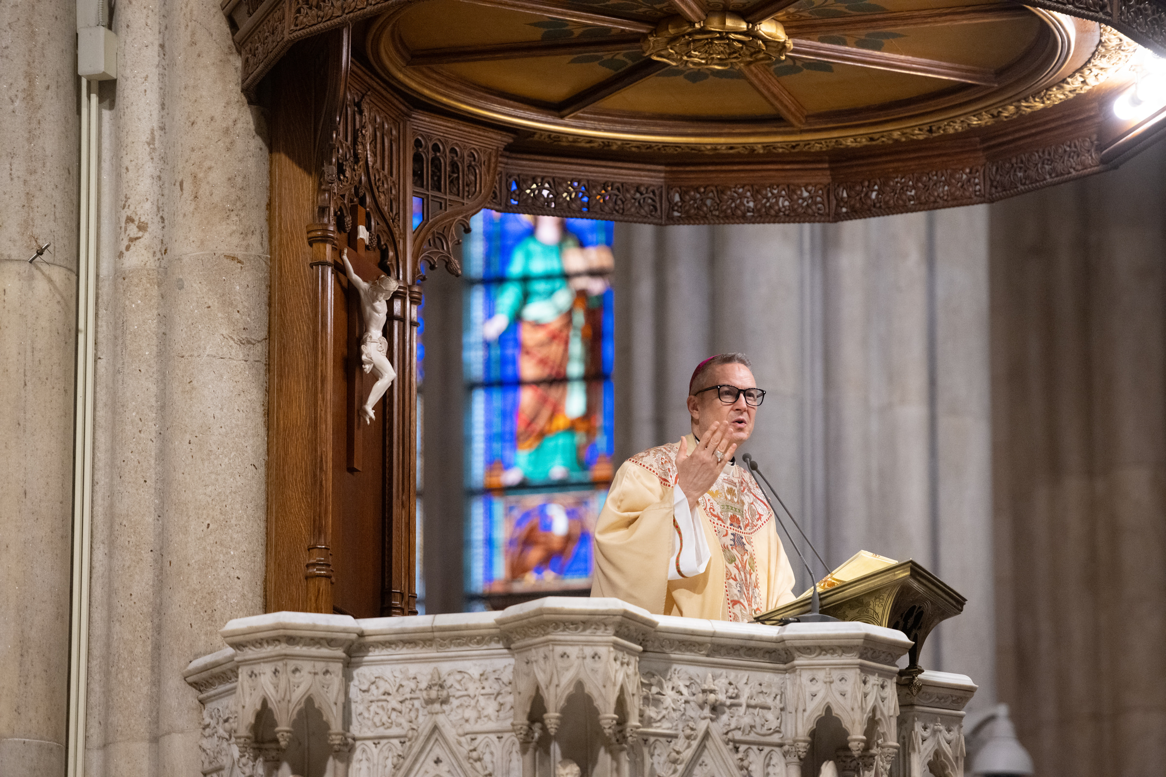 Archbishop Hicks delivers the homily from the cathedral ambo beneath a carved crucifix.