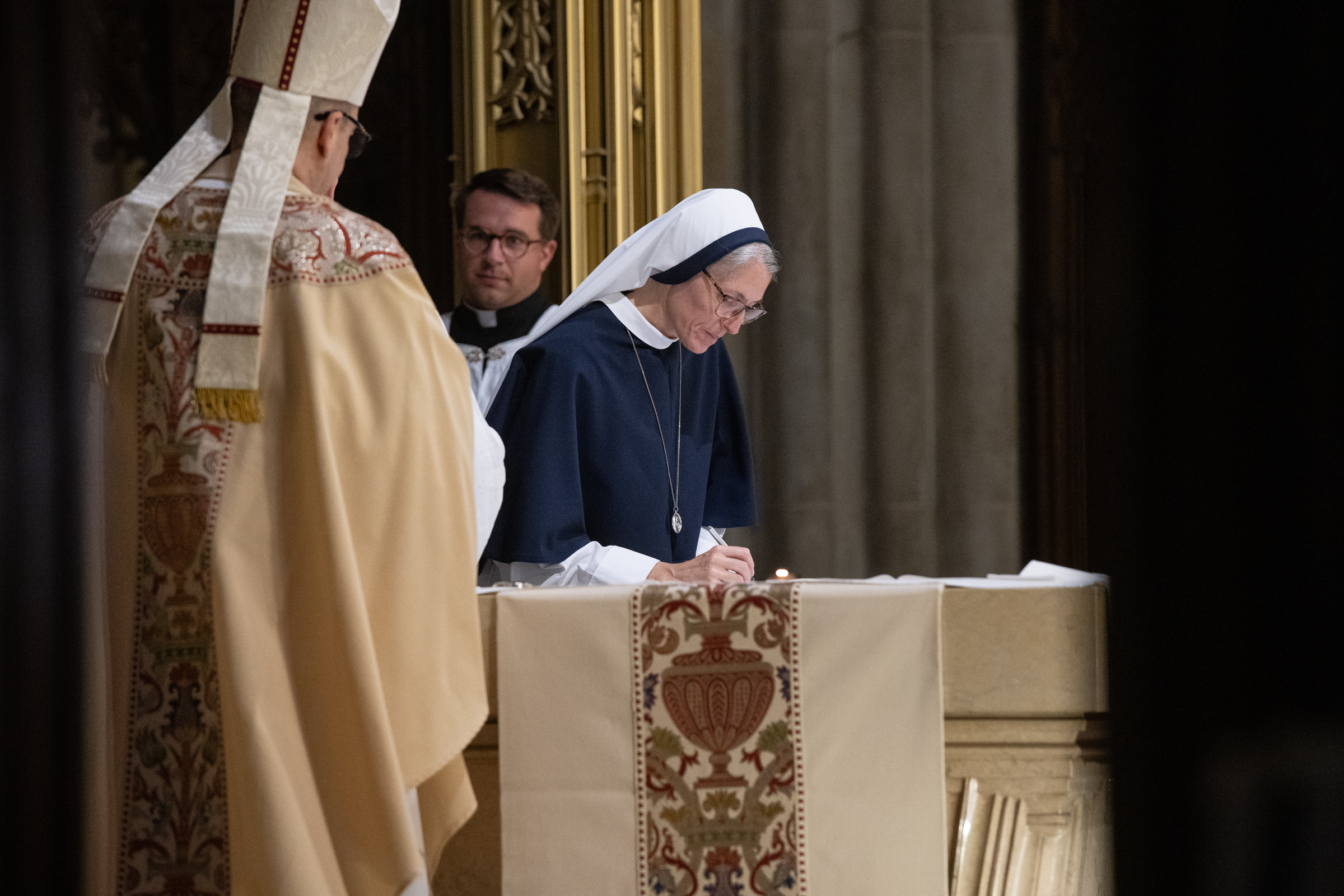 Mother Mary Concepta signs the profession record at the altar as Archbishop Hicks looks on.