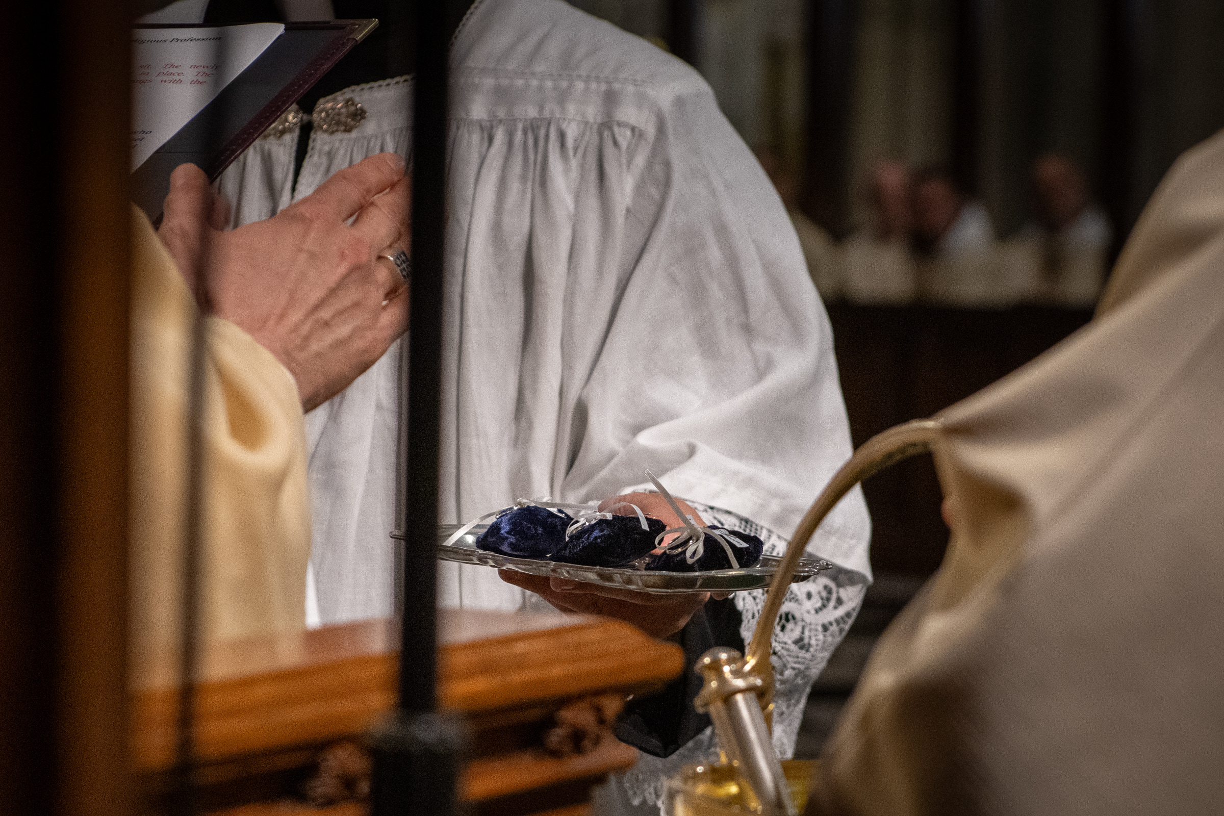 Three profession rings rest on blue velvet cushions held by an altar server.