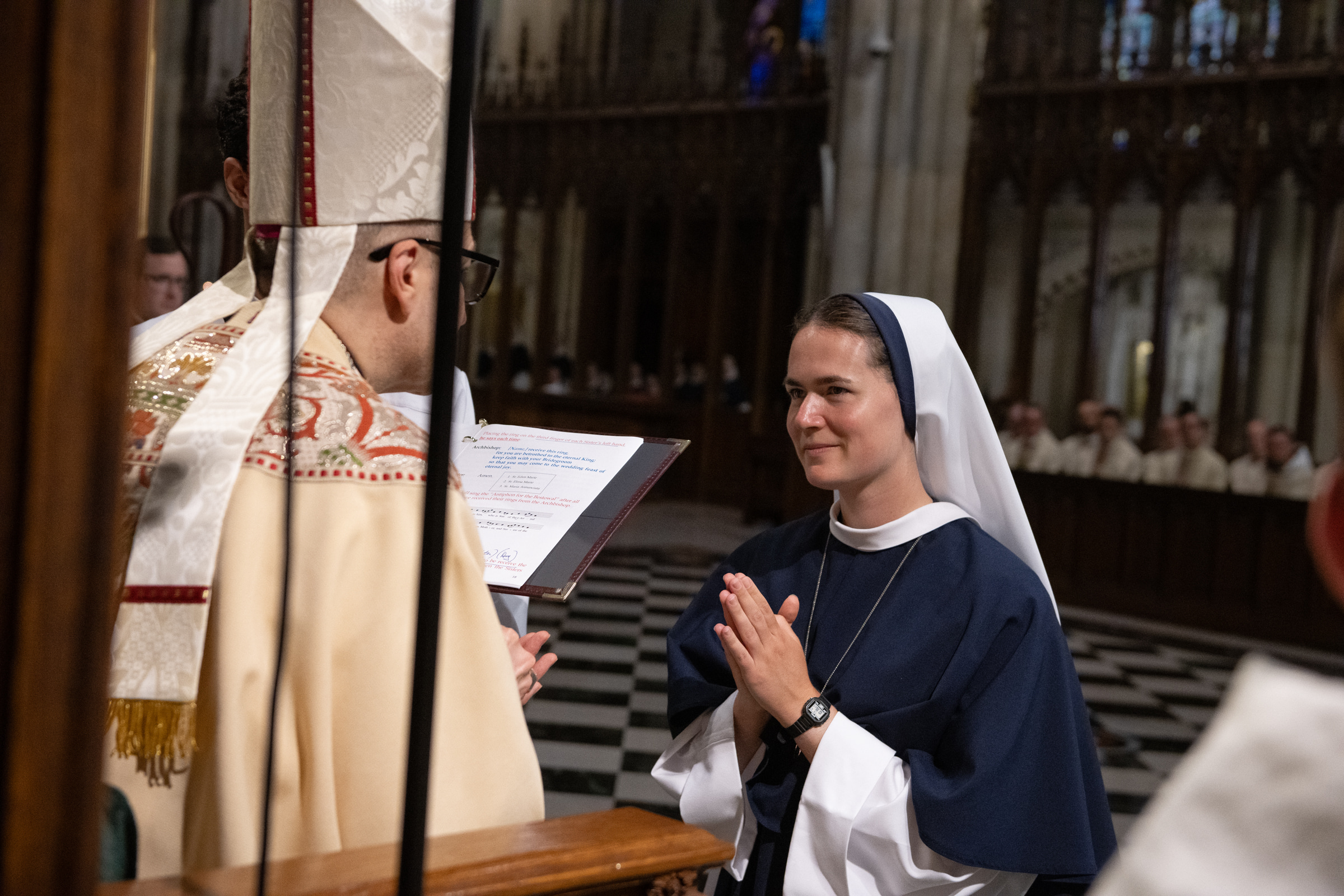 Sister Maria Annunciata, S.V., kneels before Archbishop Hicks to receive her profession ring.