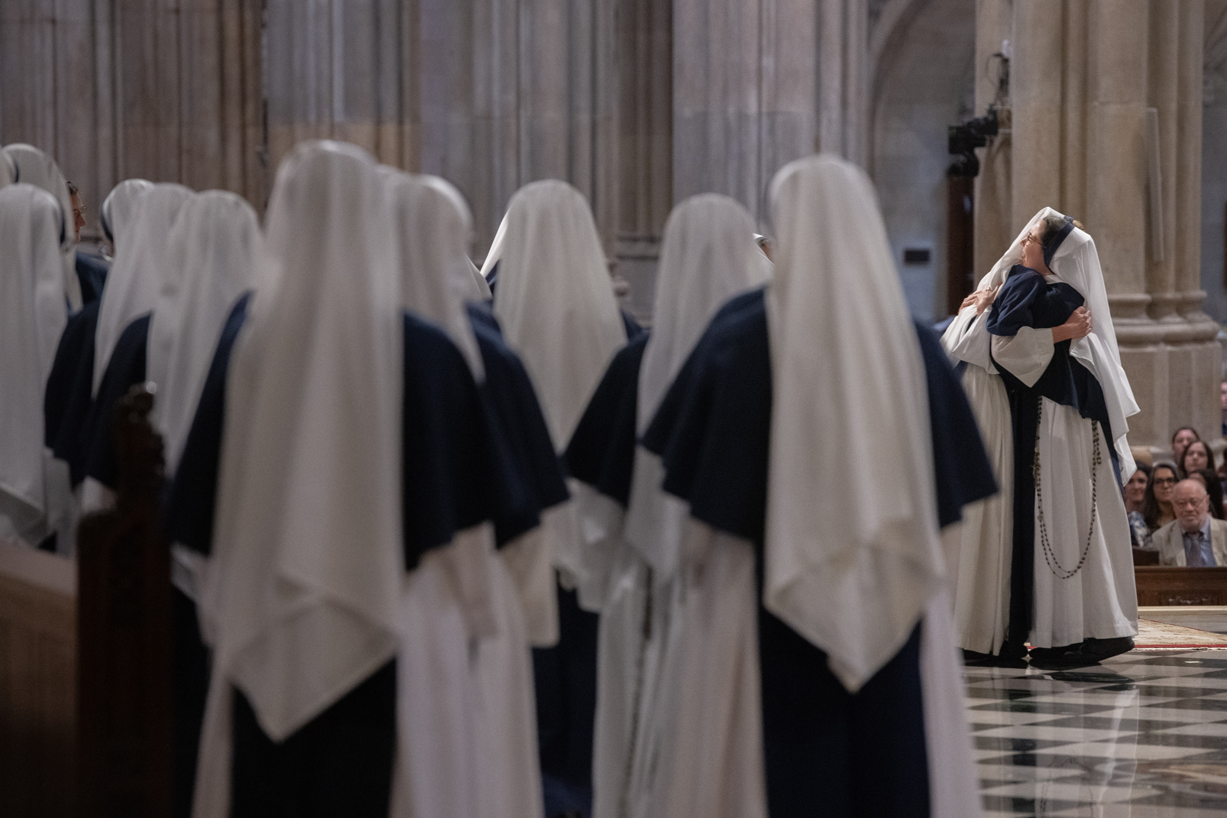 Two Sisters embrace at the front of the cathedral as the community looks on.