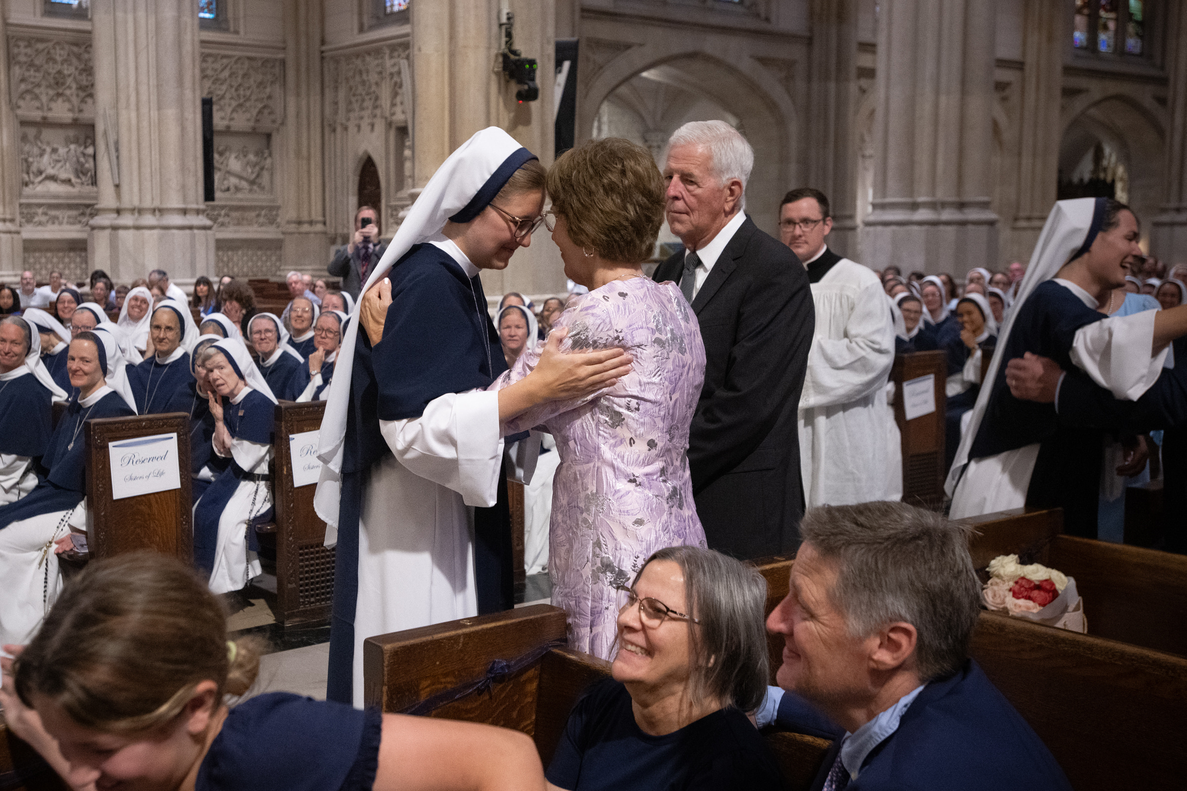 Sister Elena Marie, S.V., embraces a woman as a man stands beside them in the cathedral aisle.