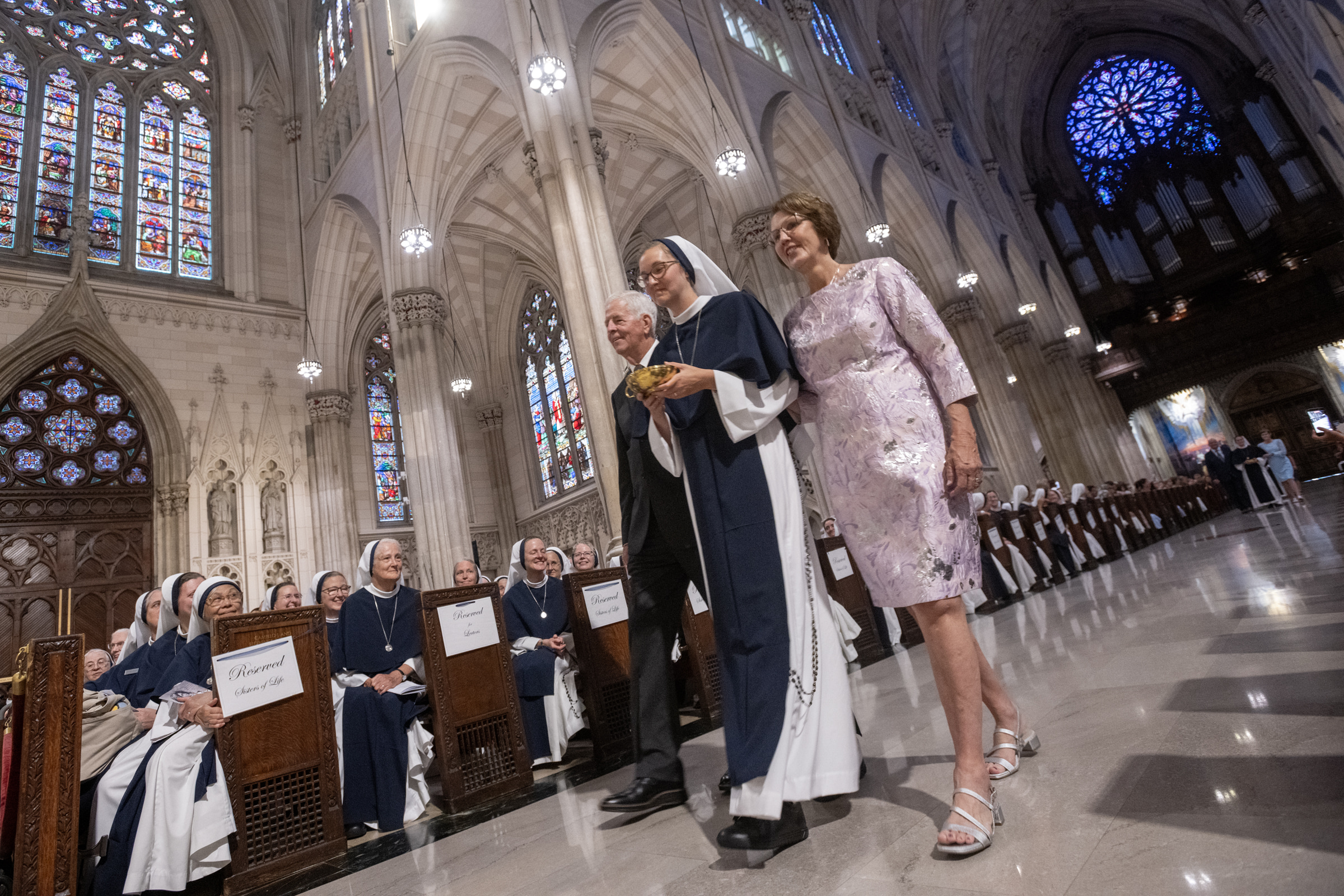 Sister Elena Marie, S.V., walks between two guests carrying a gold liturgical vessel in the offertory procession.