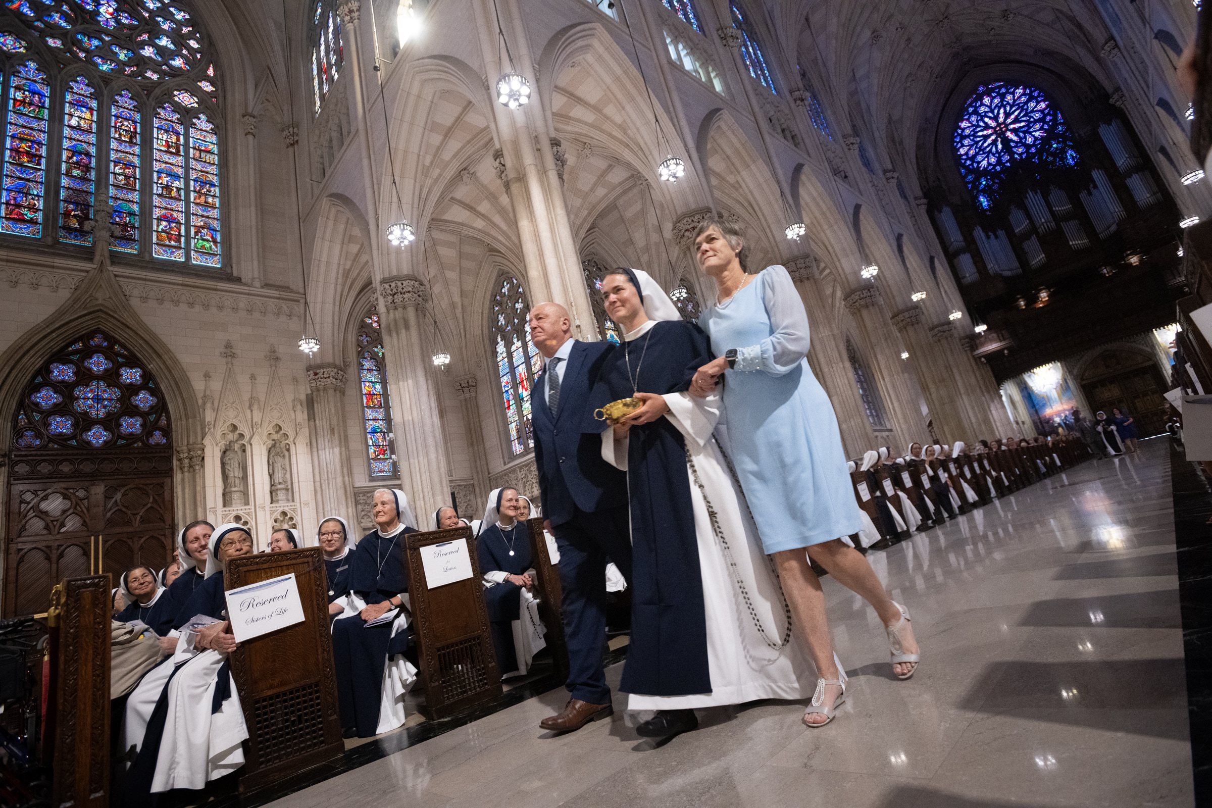 Sister Maria Annunciata, S.V., carries a gold liturgical vessel between two guests in the offertory procession.