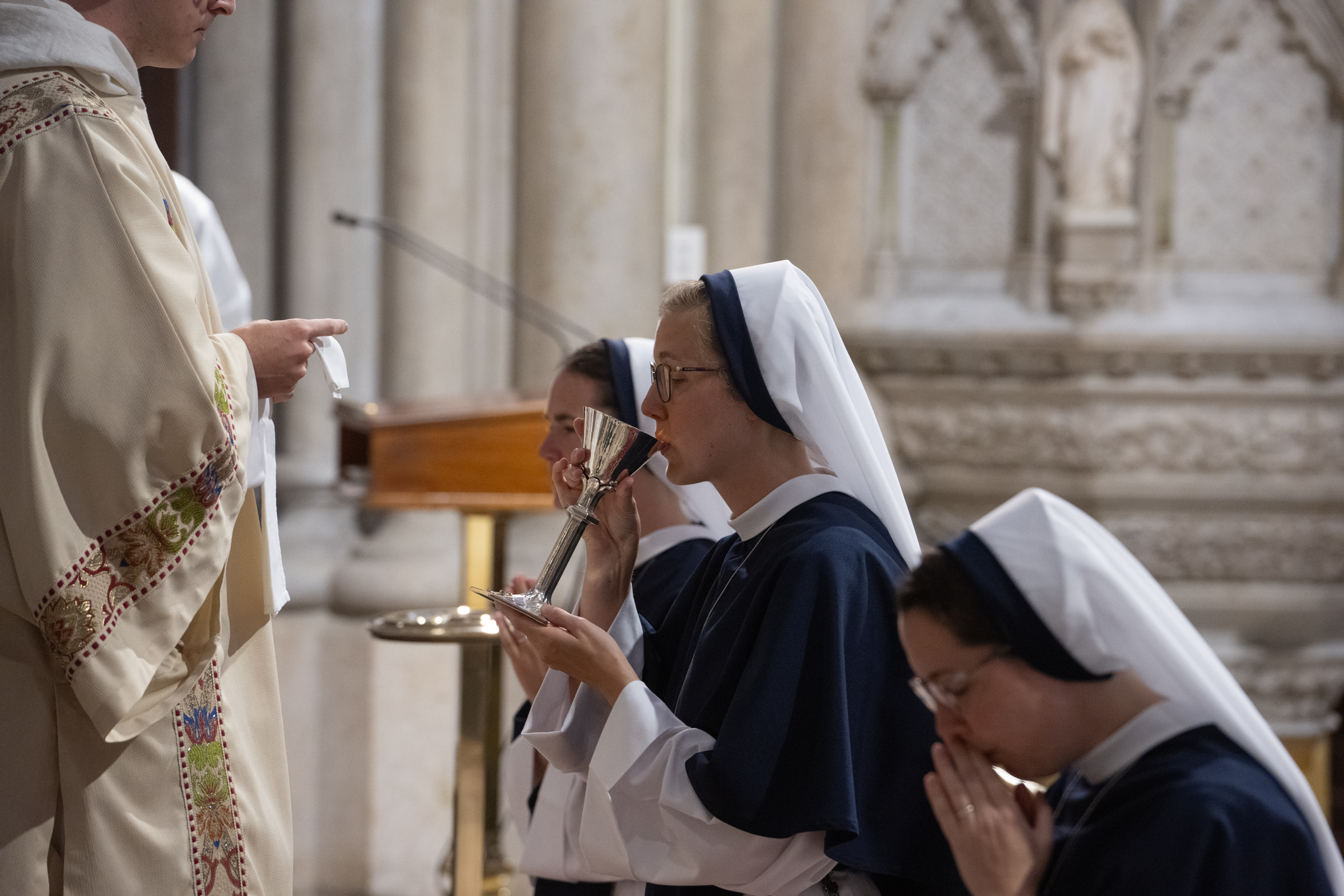 Sister Elena Marie, S.V., drinks from the chalice during Communion as another Sister kneels nearby.