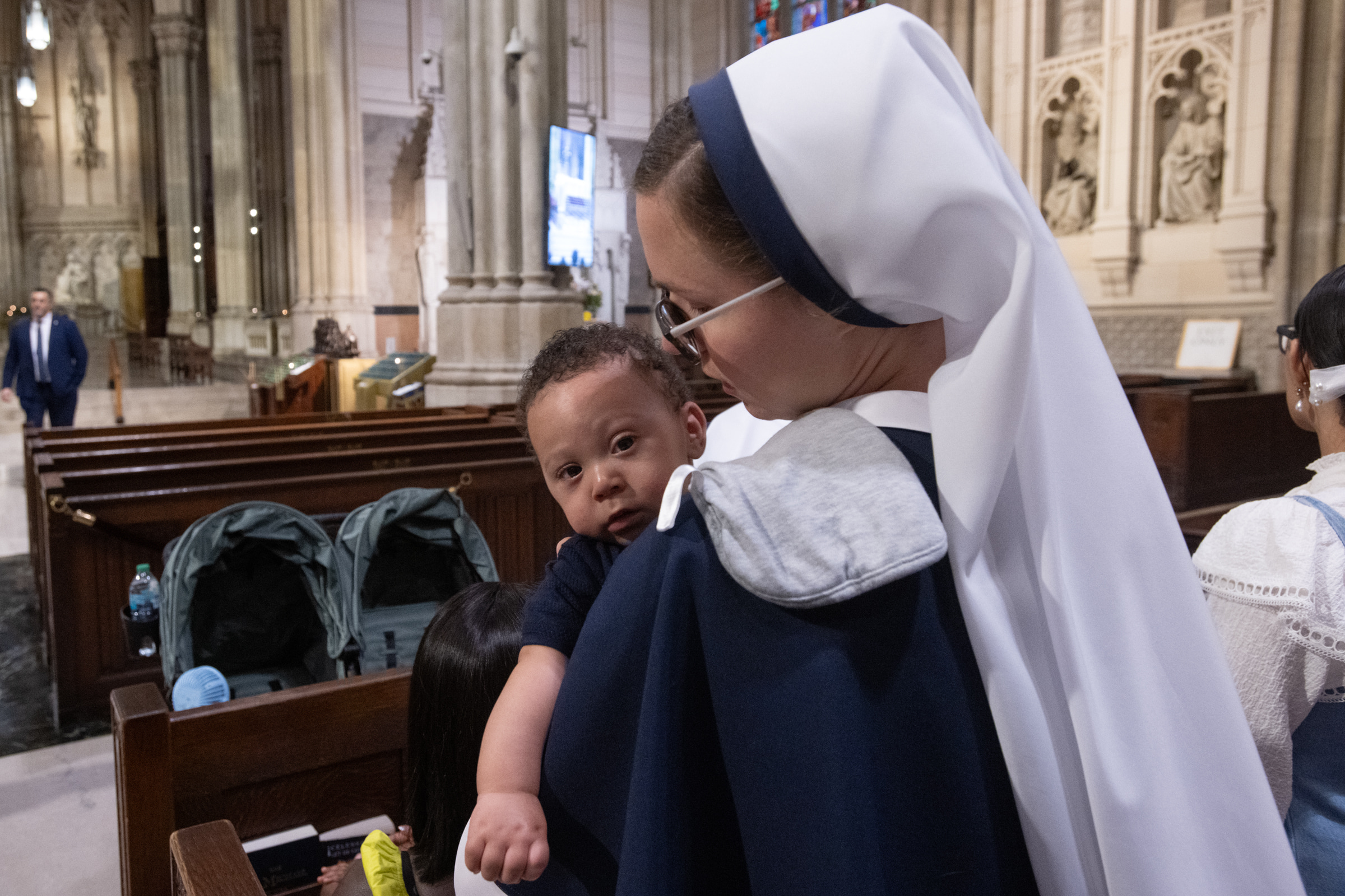 A Sister of Life cradles an infant against her shoulder in a cathedral pew.